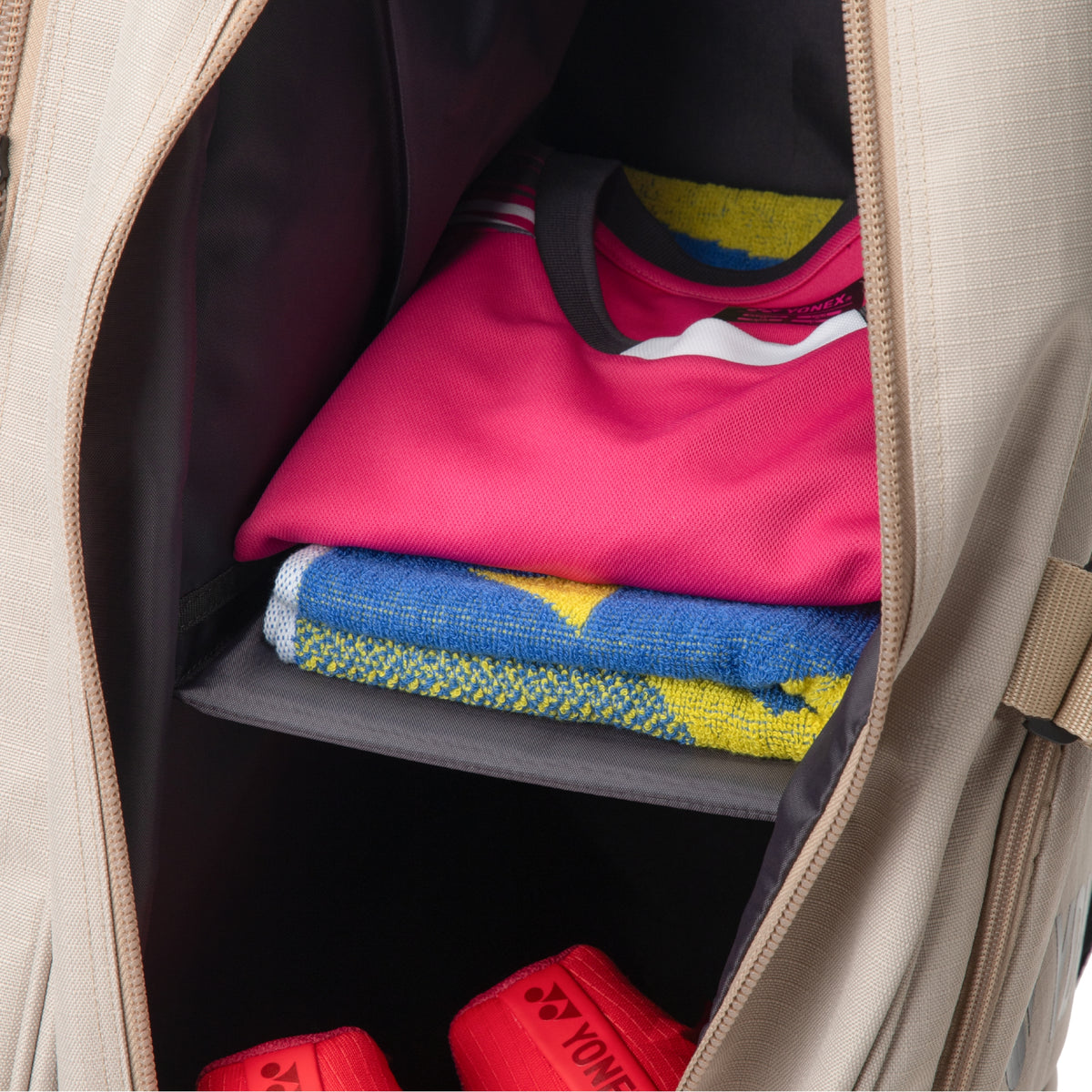 Open tennis bag with folded clothes including a pink shirt and colorful towel.