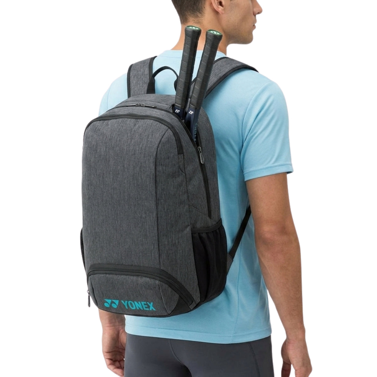 Person wearing a gray backpack with Yonex branding, holding tennis rackets.