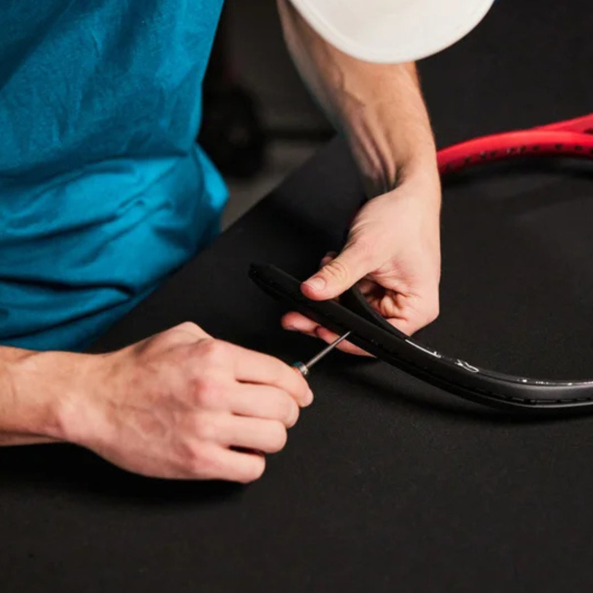Person repairing a tennis racket with a tool on a black surface