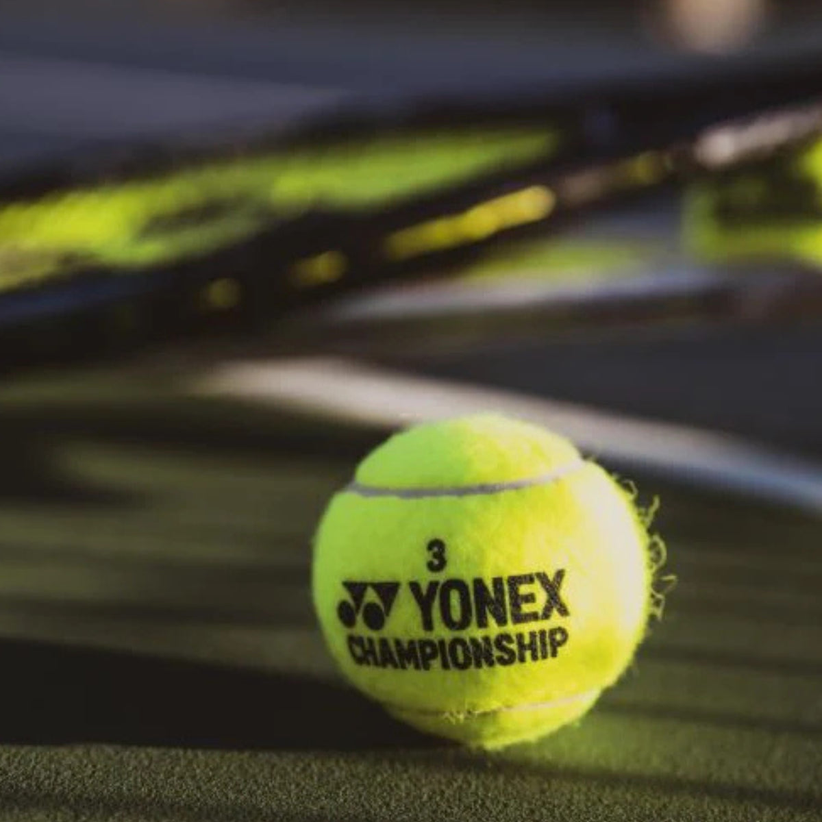 Yonex tennis ball on a tennis court with blurred rackets in the background