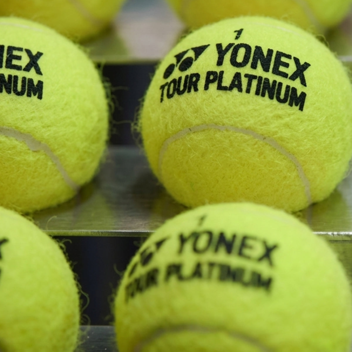 Close-up of Yonex Tour Platinum tennis balls on a metal surface.